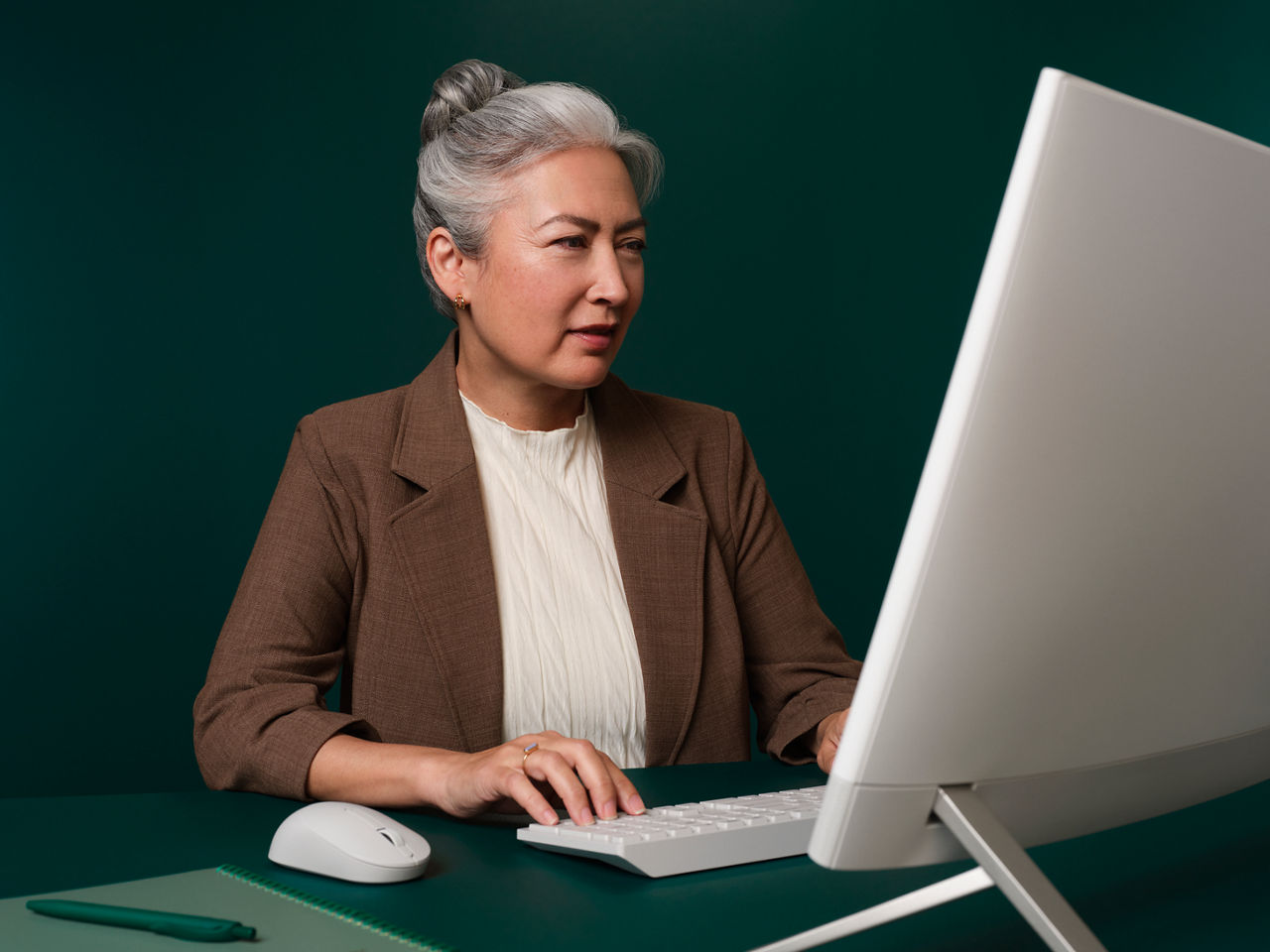 Mujer sentada en su oficina en un escritorio verde oscuro trabajando en su ordenador y mirando la pantalla.