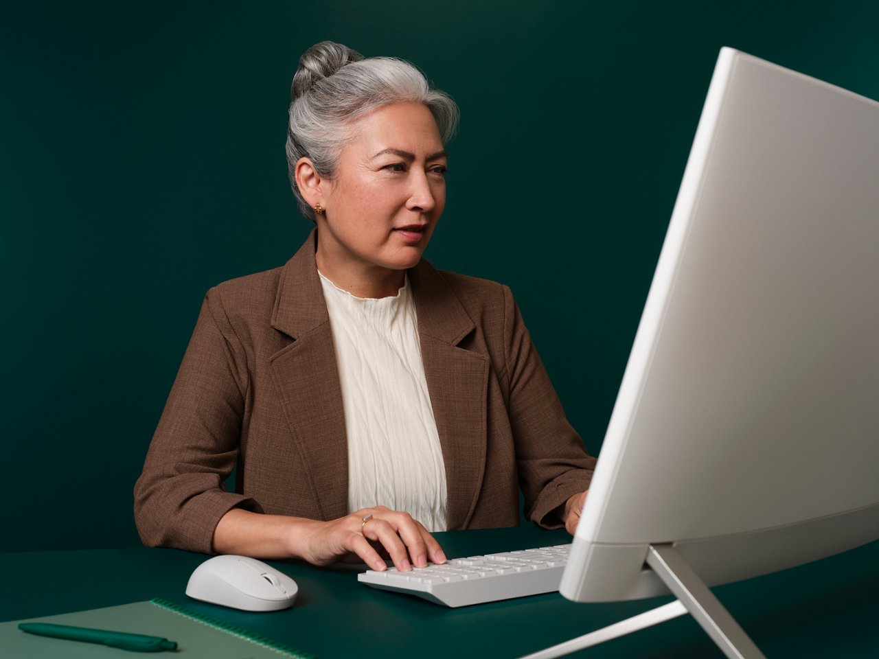 Mujer sentada en su oficina en un escritorio verde oscuro trabajando en su ordenador y mirando la pantalla.