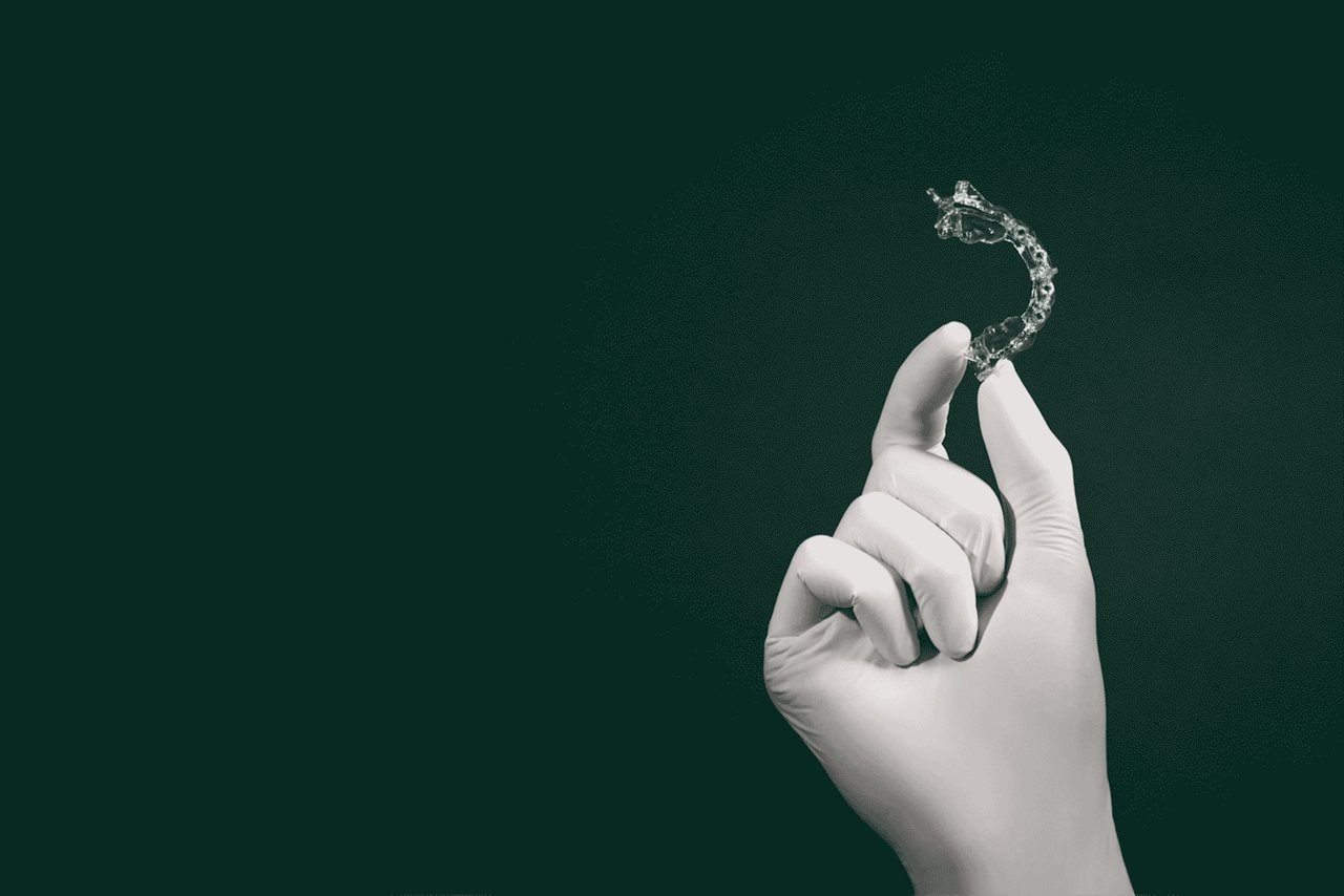 White gloved hand holding up Filtek Matrix on a dark green background.