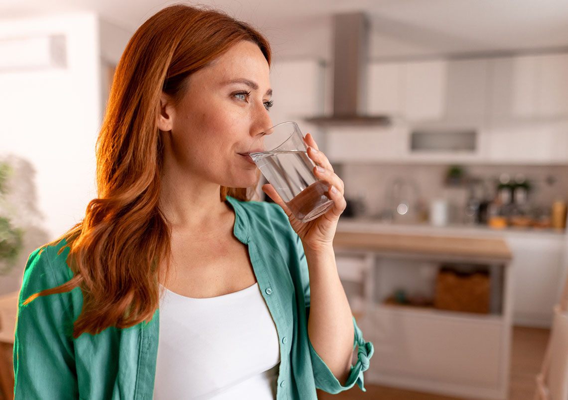A profile of a woman drinking water from a glass in a modern kitchen setting