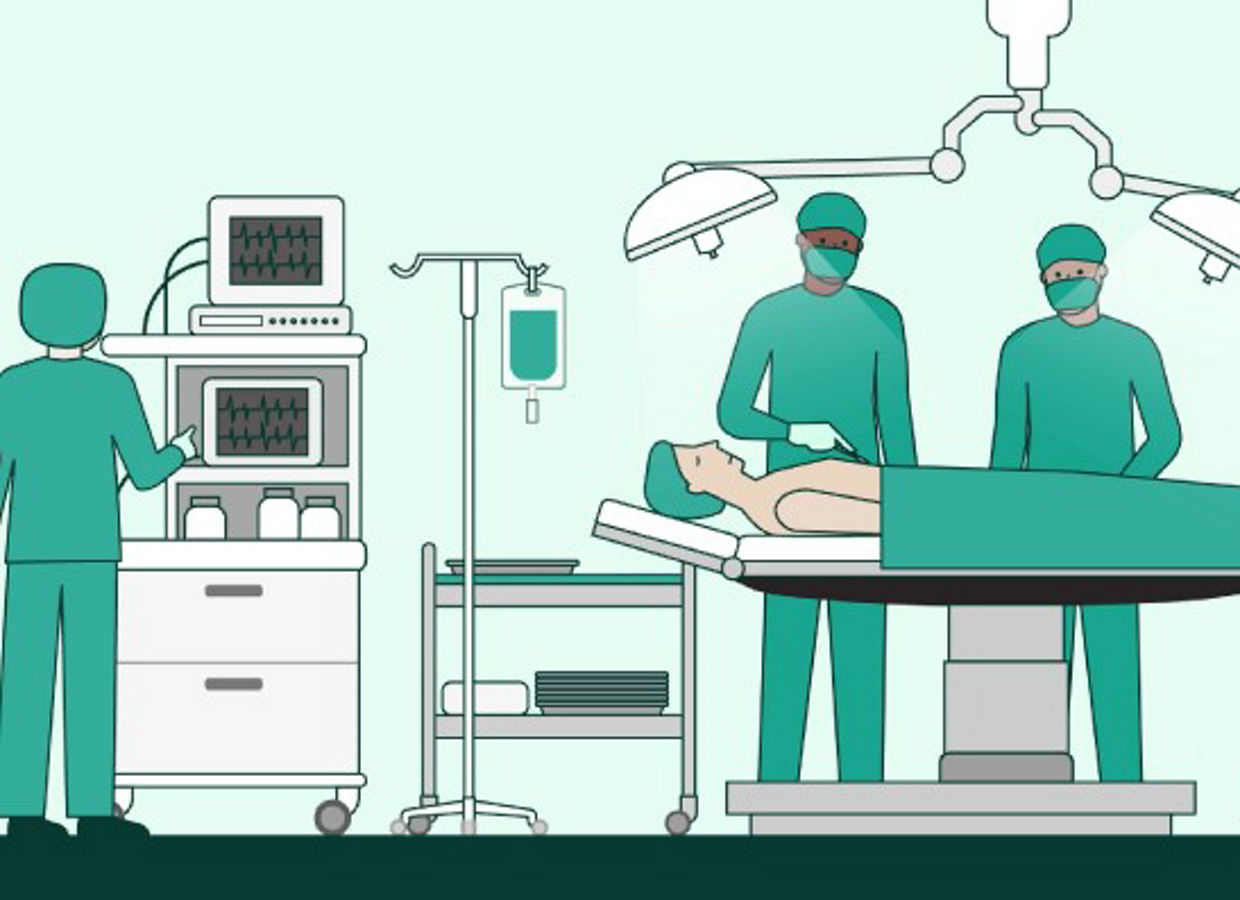 Image of a scene in the Sterilization Instrument Cycle video. On the left side, a person in green scrubs is looking at two monitors. In the rest of the image, there are two carts and an IV pole. There is a patient laying on an operating room table wearing a green blanket and two operating room lights above. Two surgeons wearing green scrubs are standing behind the patient. The surgeon on the left is holding a scalpel.