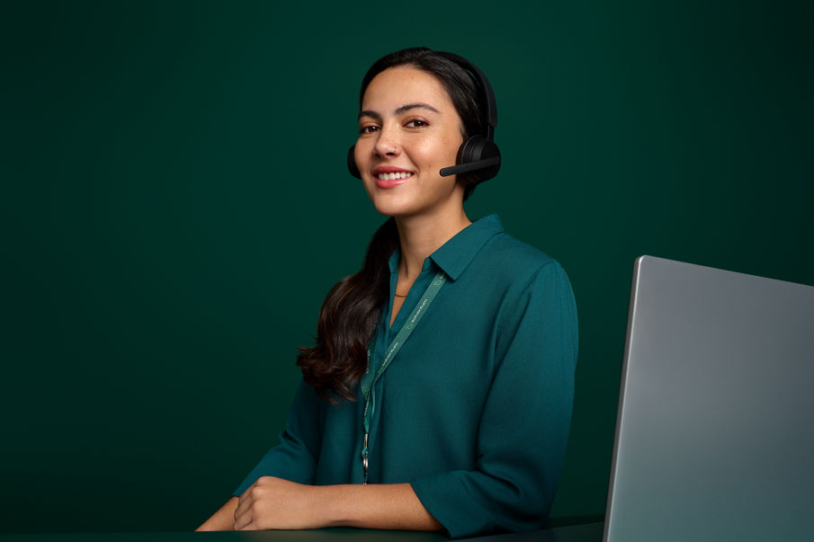 Portrait of a female call center employee smiling, seated at her desk from the Costa Rica office on a dark green background.