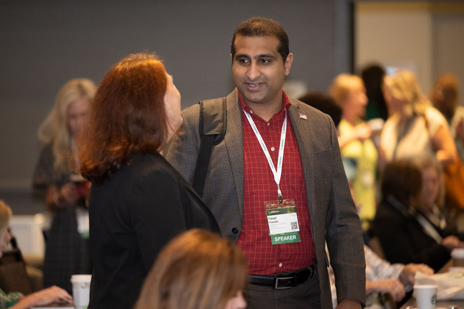 A male in a red shirt and brown jacket and female in a black suit jacket having a conversation at the 2025 Solventum CES.