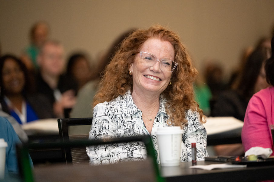 Seated woman with red hair smiling wearing a floral top.