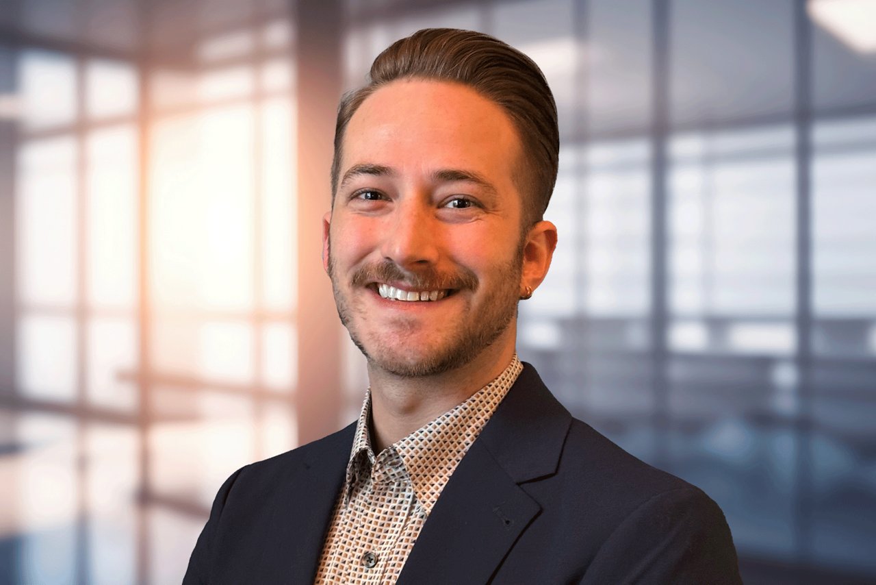 David Bowers head shot, a man with a beard, smiling in a professional shirt and black jacket against and office background.