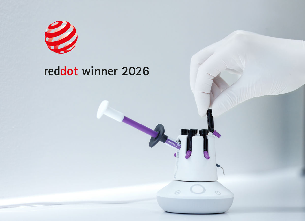 Reddot Award banner 2400x1800, gloved hand inserting a purple composite syringe into a white composite warmer device that holds multiple syringes with purple tips.