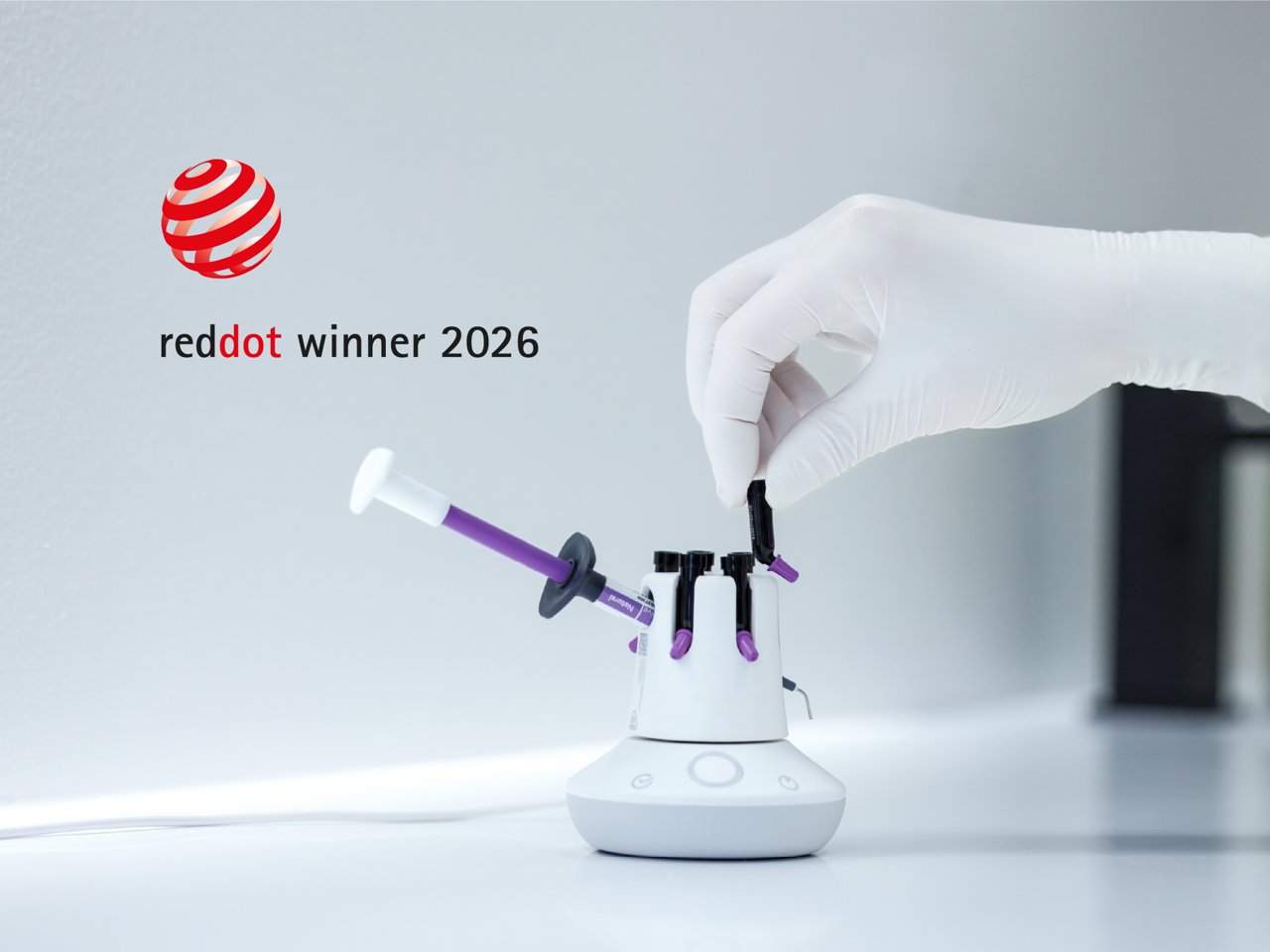 Reddot Award banner 2400x1800, gloved hand inserting a purple composite syringe into a white composite warmer device that holds multiple syringes with purple tips.