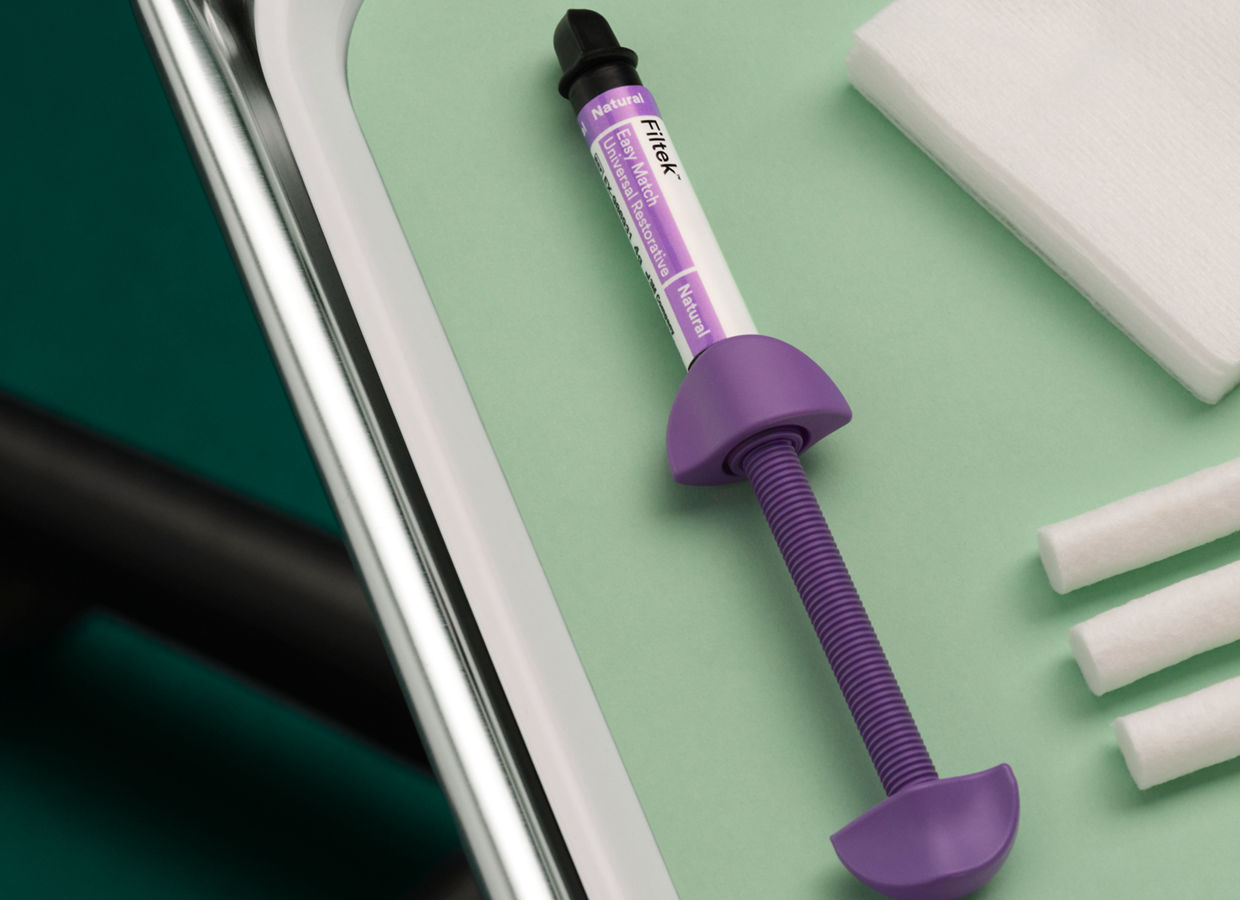 La seringue 3M Filtek Easy Match Universal Restorative repose sur un plateau de dentiste en métal avec un insert en plastique blanc et une doublure vert clair, le fond du sol est vert foncé.