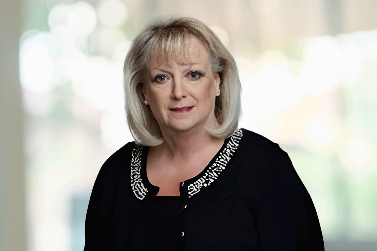 Head shot of a woman wearing a black cardigan set against an office background.