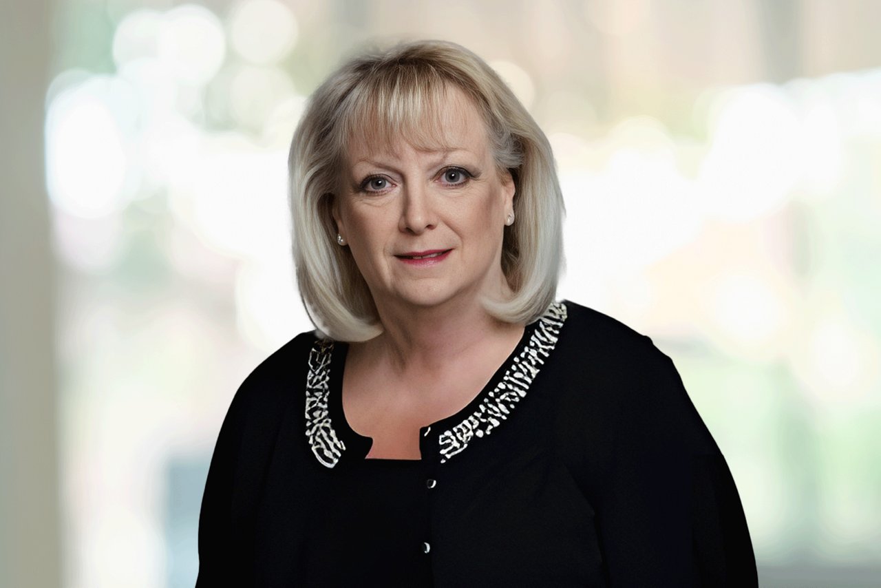 Head shot of a woman wearing a black cardigan set against an office background.