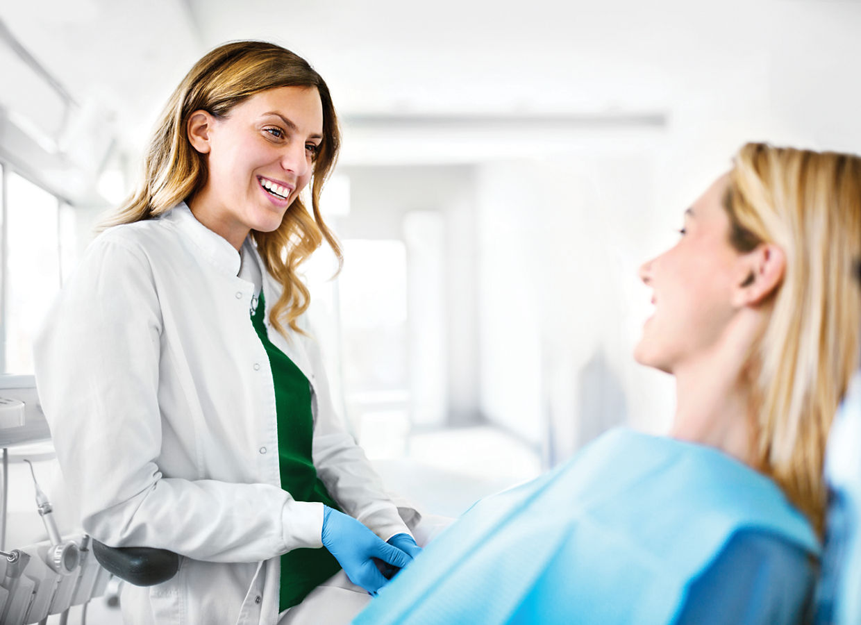 Photo of a female orthodontist having a conversation with a happy young female patient in an orthodontist clinic.