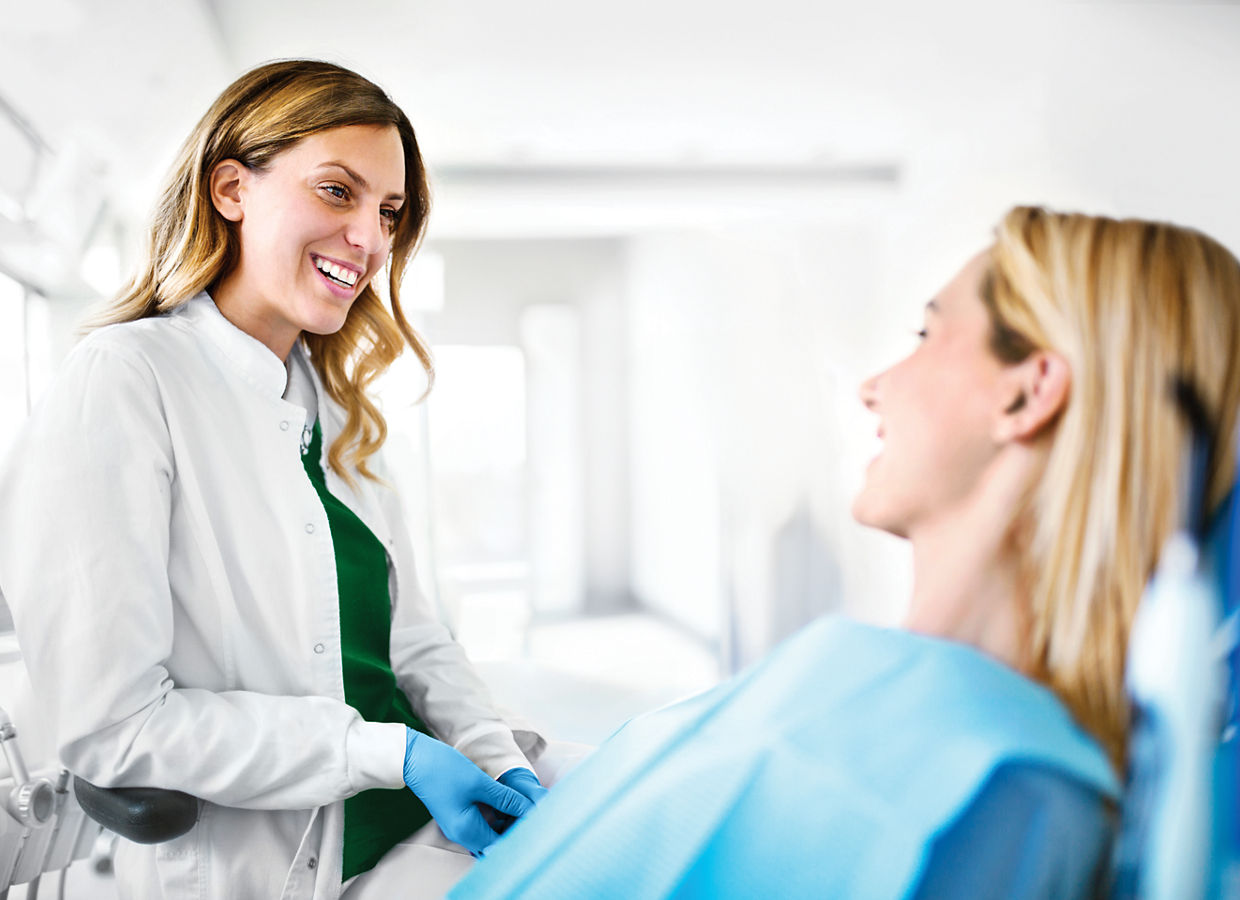 Foto van een vrouwelijke orthodontist die in een orthodontische praktijk met een vrolijke jonge patiënte in gesprek is.