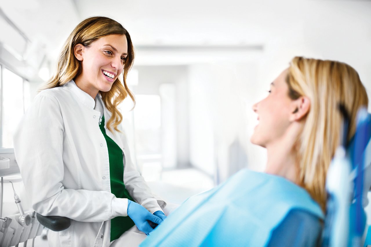 Foto van een vrouwelijke orthodontist die in een orthodontische praktijk met een vrolijke jonge patiënte in gesprek is.