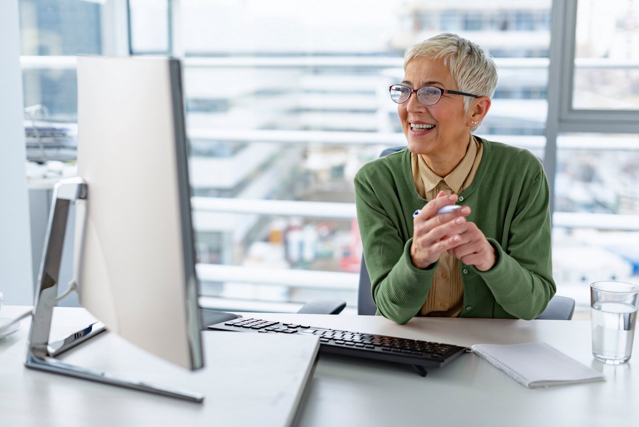 Confident senior businesswoman smiling while working at her desk on a computer in a bright, modern office during the day.