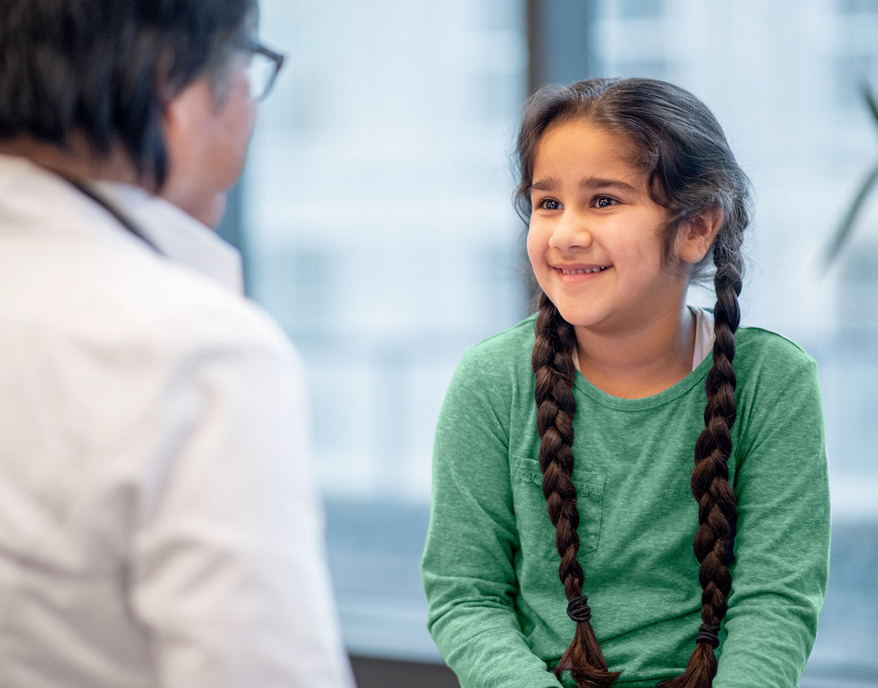 A mature doctor talks with a smiling young girl during a routine check-up in his office.