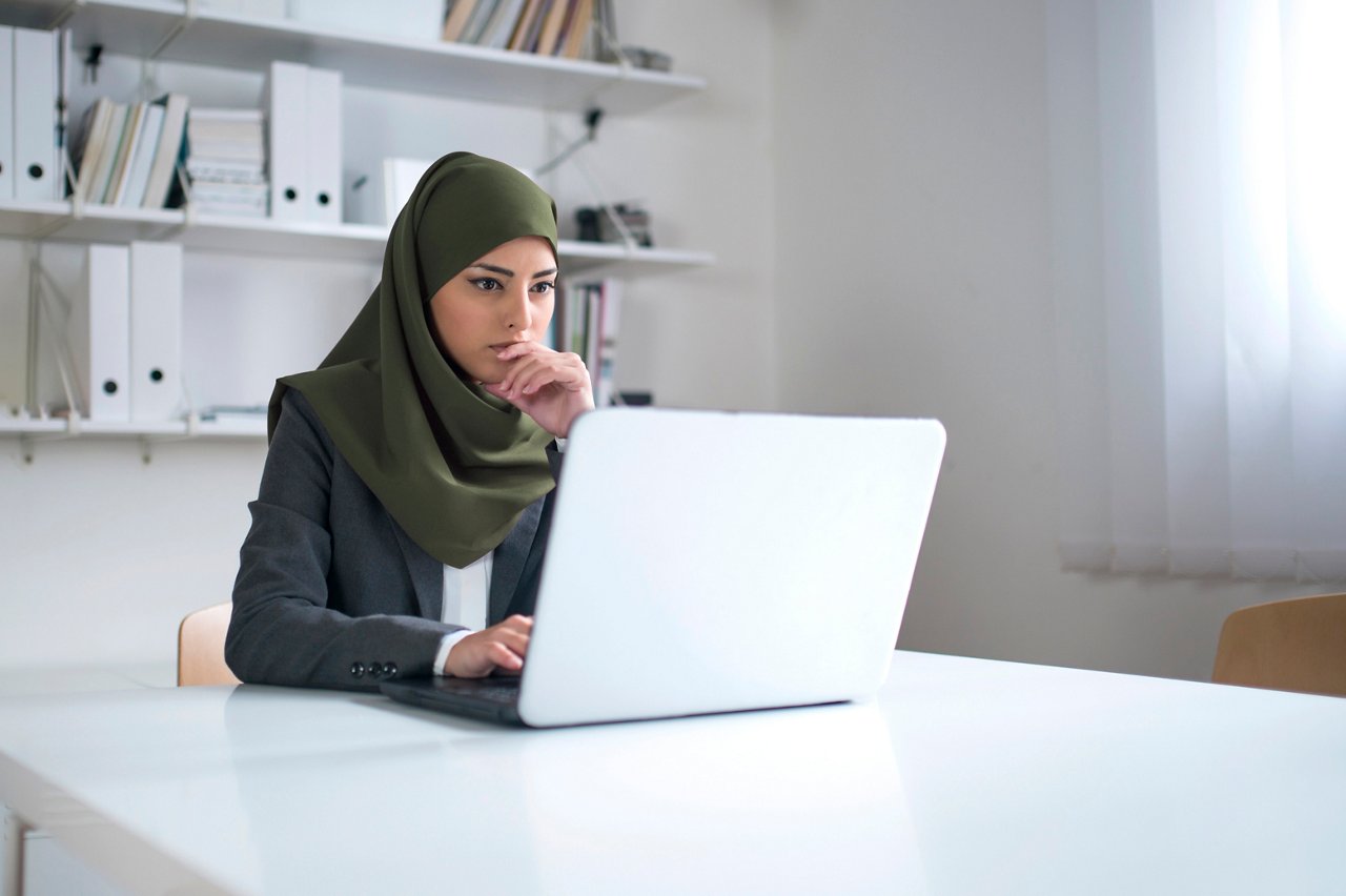 Business woman with hijab works on her laptop in an office.