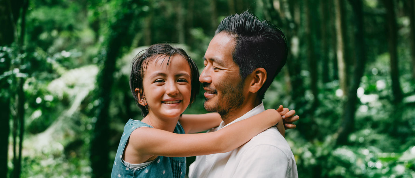 Japanese father and his young mixed race daughter cuddling in lush green rainforest, Tanegashima Island, Kagoshima, Japan