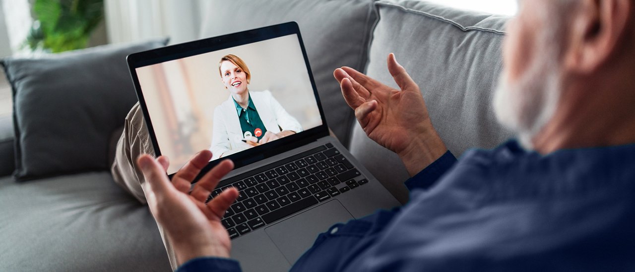 En mand, der sidder på sofaen og taler med sin læge under et telesundhedsbesøg.