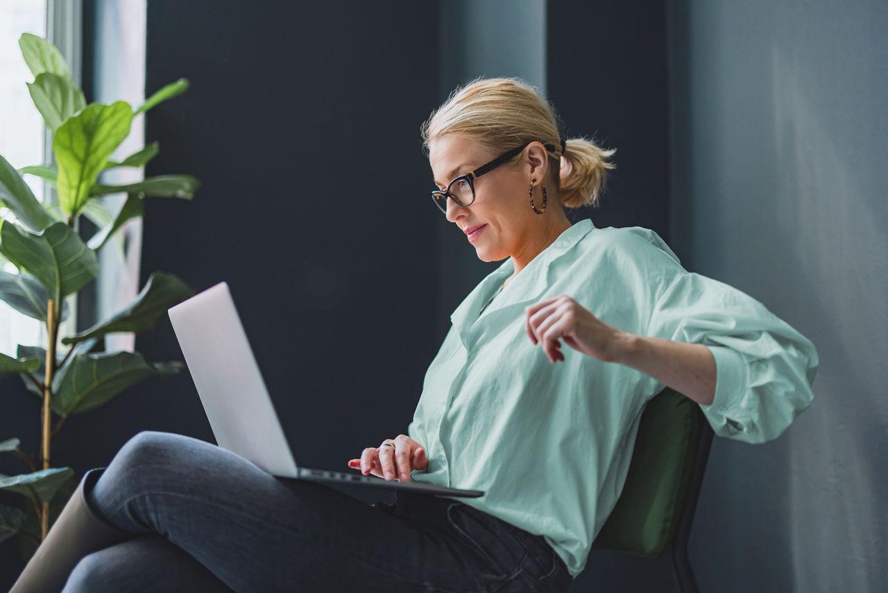Smiling business woman sitting on a chair and working on a laptop.