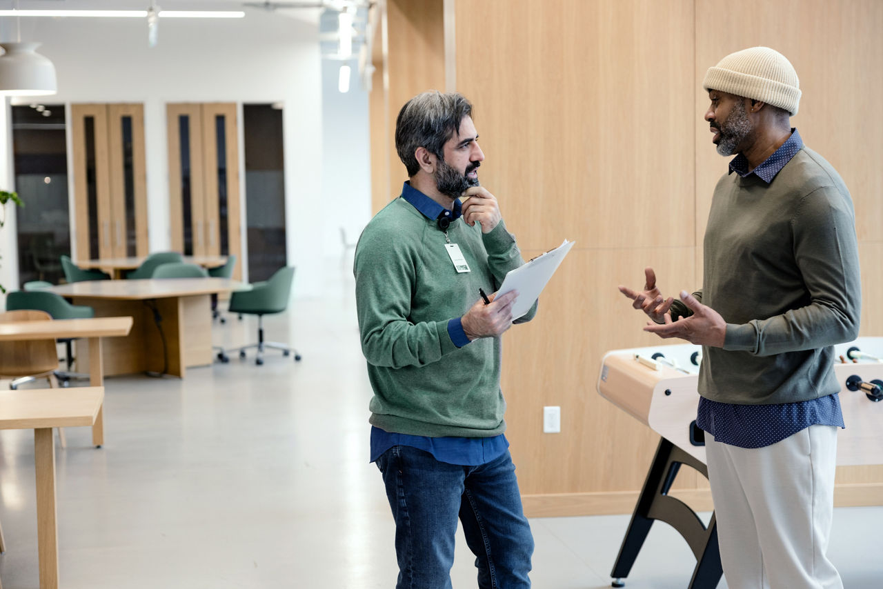 A male doctor meets with his African patient, both dressed semi‑casually, as they stand together in an office lounge area.
