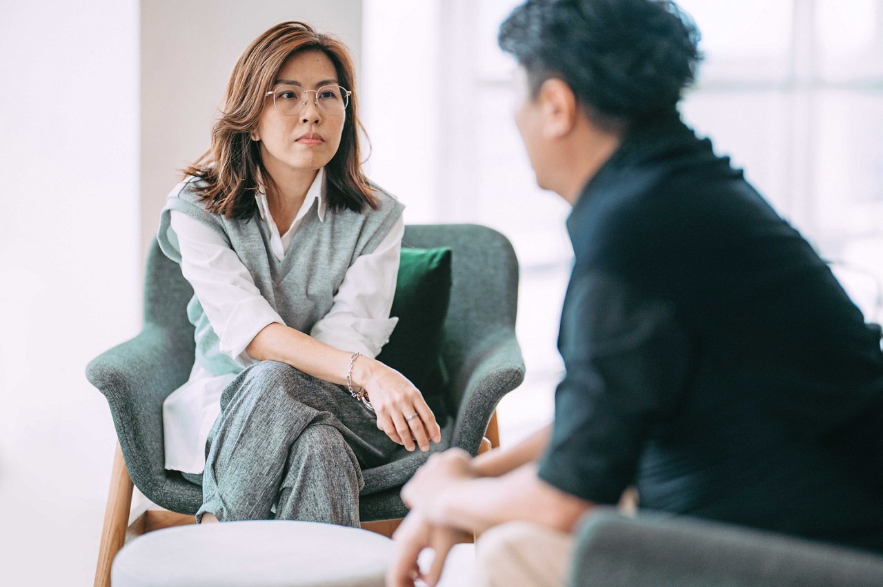 A therapeutic dialogue between an Asian female psychologist and a mature man, consulting patient at a modern office.