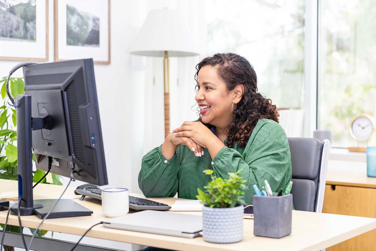 Una donna d'affari adulta sorride mentre legge un'email alla scrivania in un ufficio moderno.