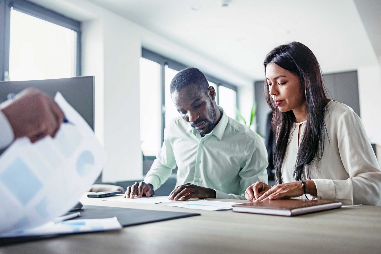 Black and Latin business professionals collaborate in an office, demonstrating teamwork and professionalism in a naturally lit modern office.