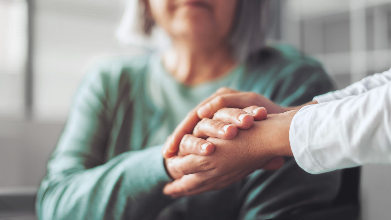 Close-up of doctor's hands holding mature woman's hands in hospital.
