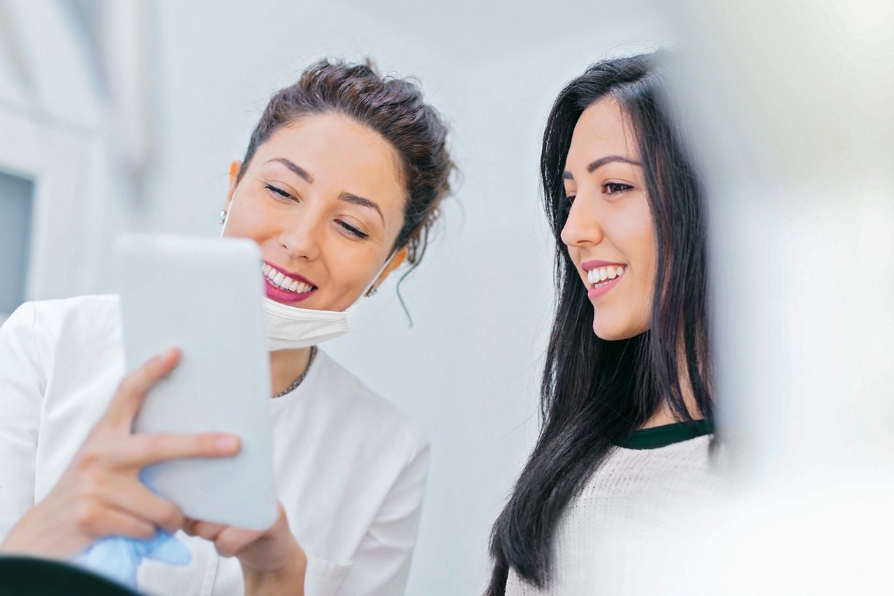 Een mondzorgprofessional en een glimlachende patiënt praten met elkaar terwijl ze samen naar het scherm van een tablet kijken.