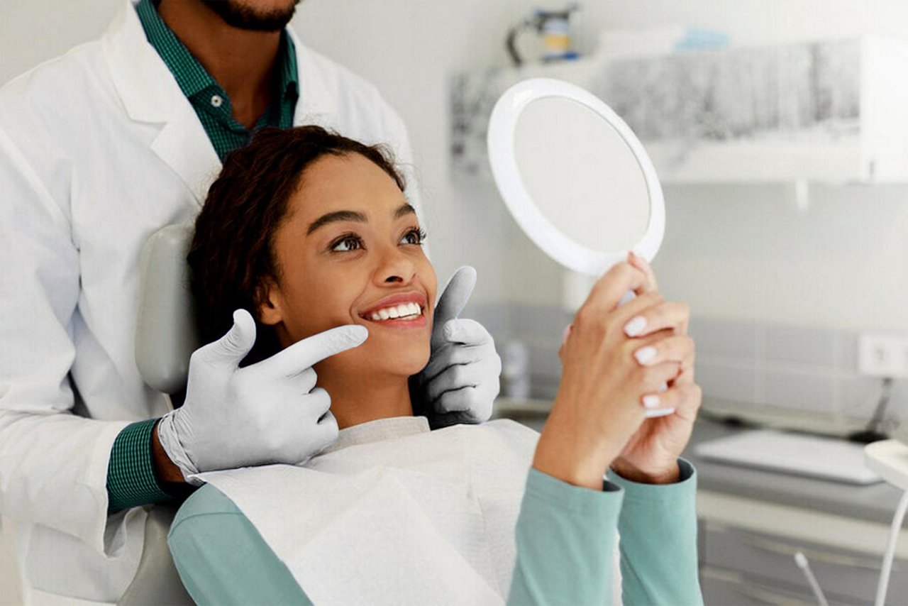 Una imagen de una mujer mirándose los dientes en un espejo de mano mientras su ortodoncista señala sus dientes