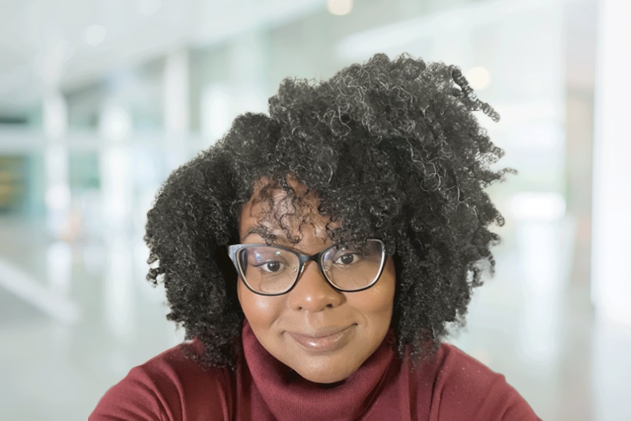 Head shot of a woman wearing glasses and a maroon sweater in an office setting.