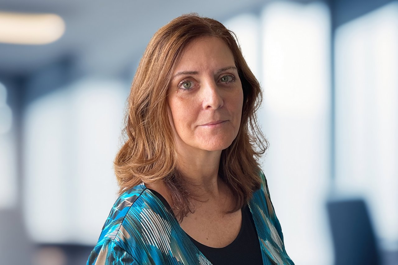 Laureen Jandroep head shot, a smiling woman with brown hair in a blue patterned shirt against an office background.
