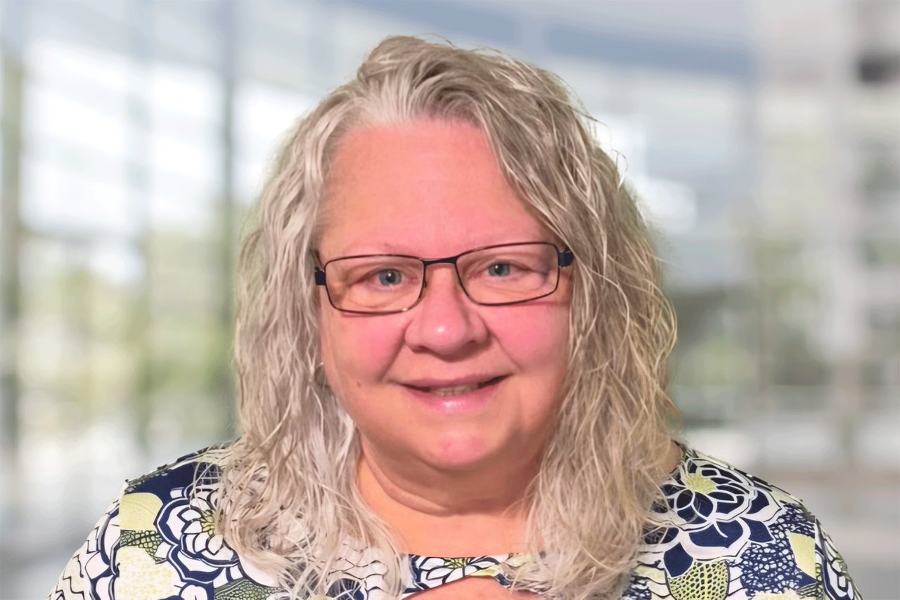 Head shot of a woman wearing glasses and a black and white shirt in an office setting.