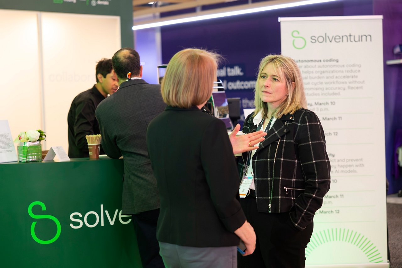 Two women standing and speaking in front of a Solventum tradeshow booth.