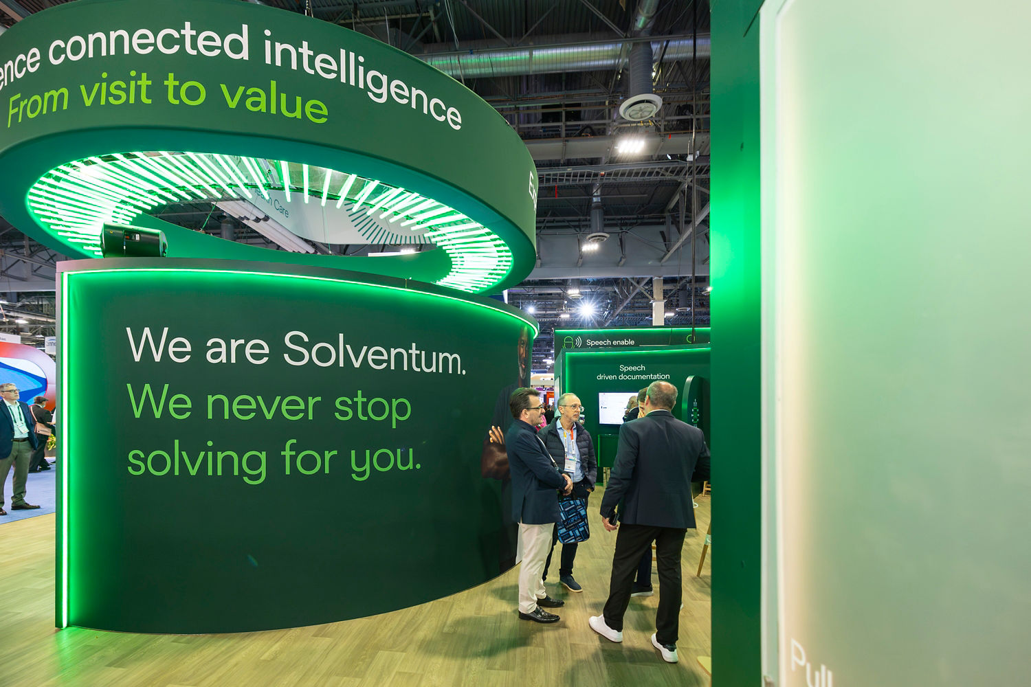A small gorup of men standing and speaking in front of a Solventum tradeshow booth.
