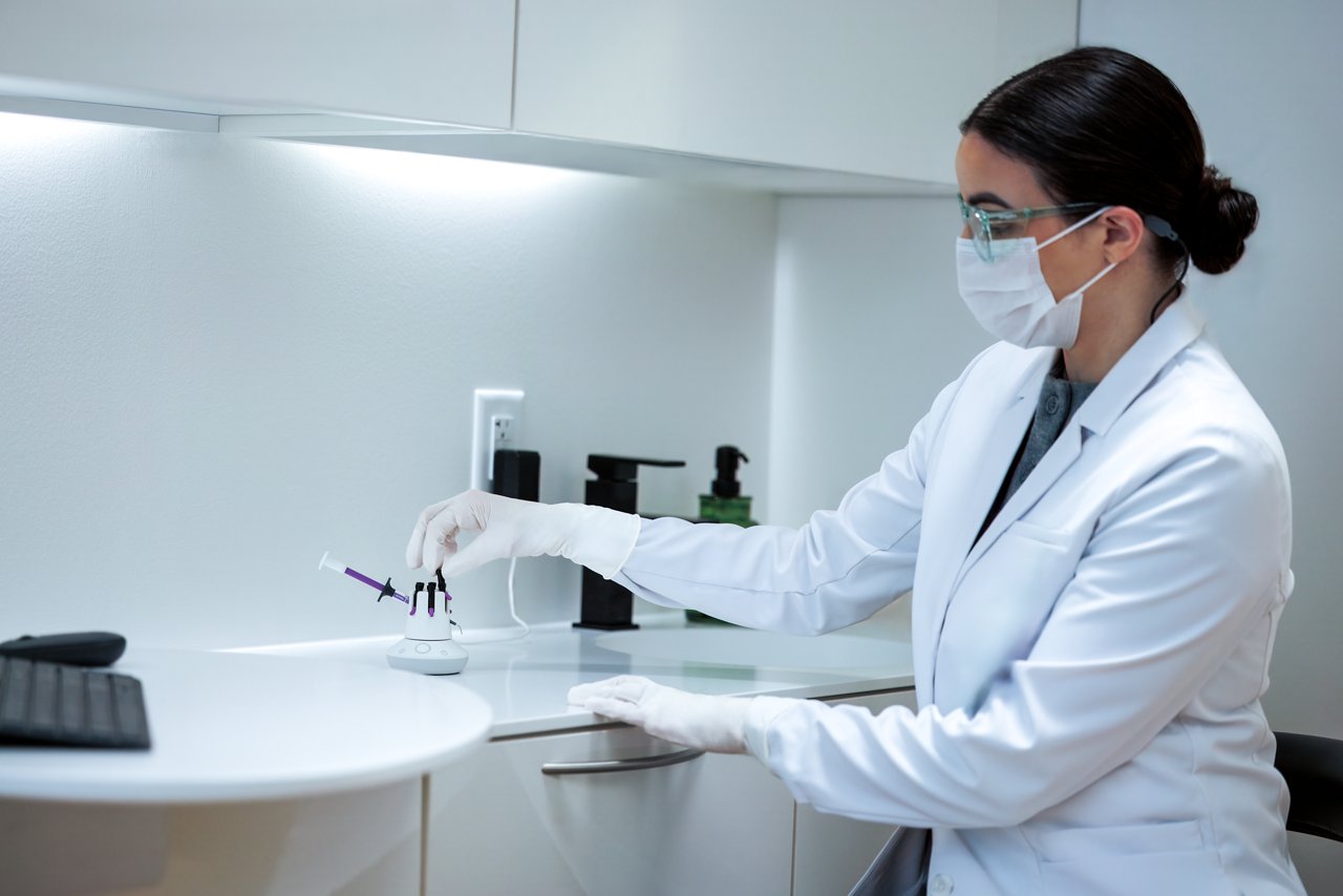 A dental professional places composite materials into a composite warming device in a clinical workspace.