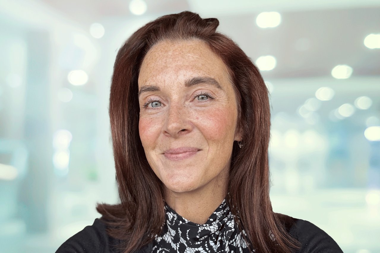 Headshot of a woman in a black cardigan and black and white shirt in an office setting.