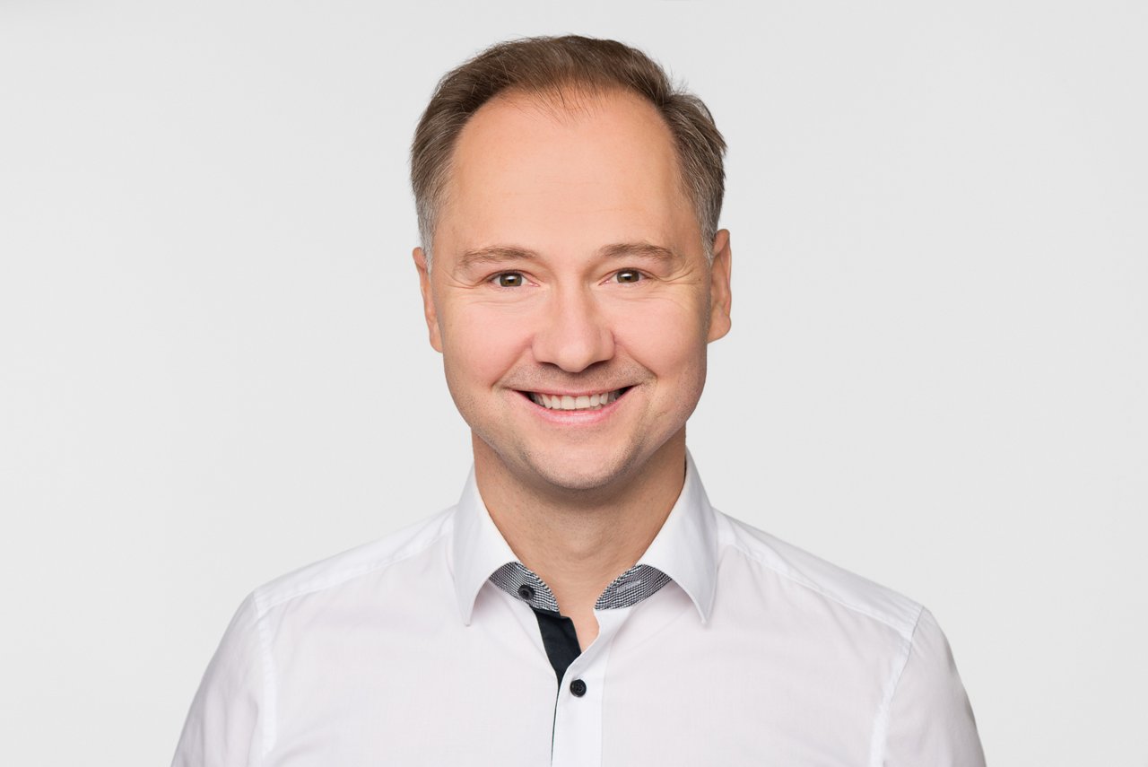 Portrait image of a person wearing a light button-down shirt against a plain light gray background.