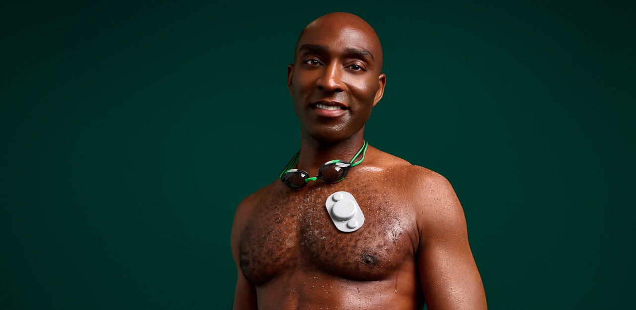Portrait of a male swimmer with a wearable device with silicone medical tape on his chest, on a dark green background.