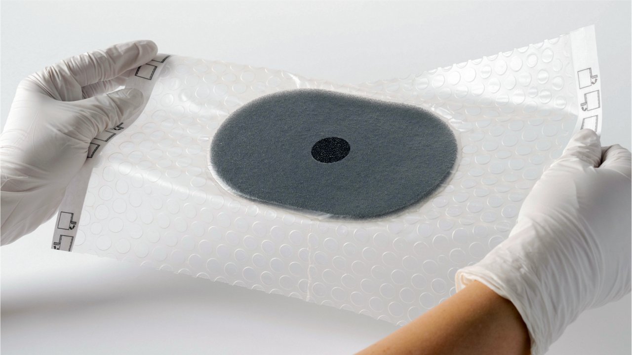 Image esthétique du pansement 3M™ V.A.C.® Peel and Place sans doublure, placé par des mains gantées de blanc sur un fond blanc.