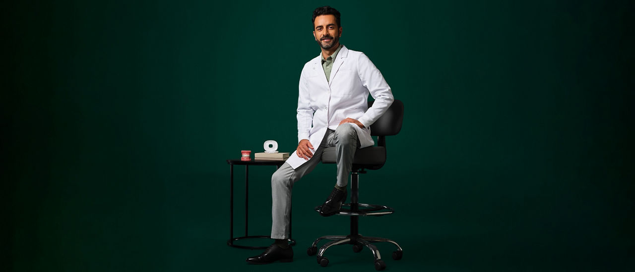 Orthodontiste masculin en blouse blanche, assis sur un tabouret près d’une petite table avec un étui aligneur et une étoile de typographe dessus