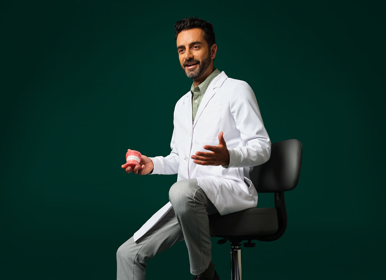 Orthodontist wearing a white coat sitting holding a typodont.