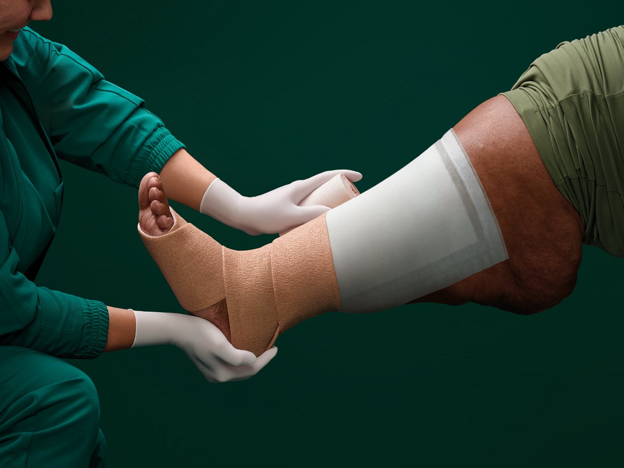 Retrato de una enfermera envolviendo la pierna de una paciente de cuidados de heridas con un apósito superabsorbente bajo la terapia de compresión sobre un fondo verde oscuro.