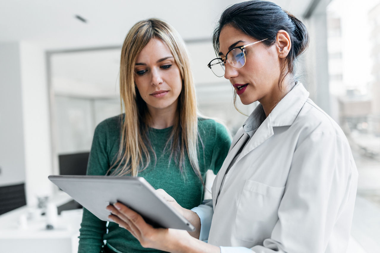 Female doctor explaining medical treatment with digital tablet to a patient during consultation.