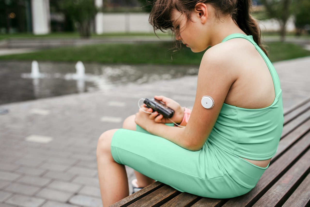 Young girl sitting on a bench while checking her wearable device on her upper arm.