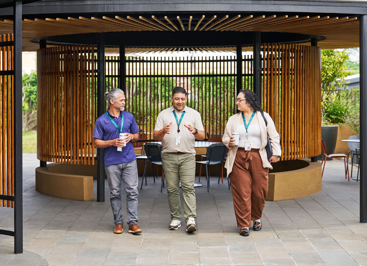 Three Solventum employees walk together under a modern outdoor pavilion with wooden slats and open seating in the background.