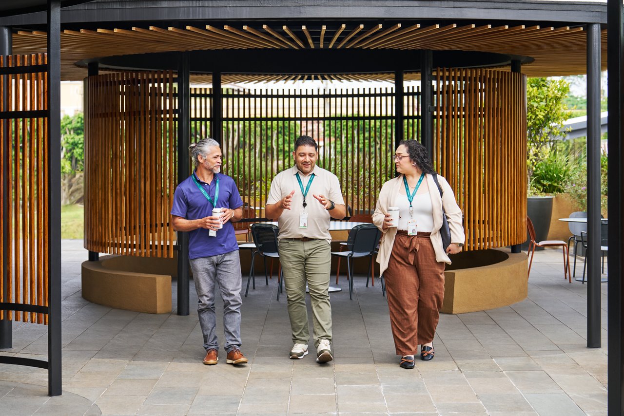Three Solventum employees walk together under a modern outdoor pavilion with wooden slats and open seating in the background.