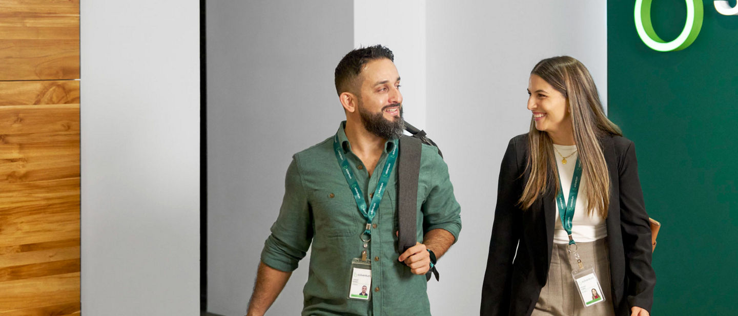 Male and female employee smiling at each other, walking through Solventum office lobby.