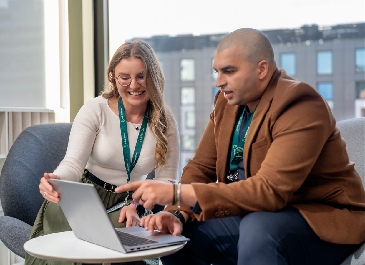 Two Solventum colleagues sit together reviewing content on a laptop during a collaborative discussion in a modern office setting.