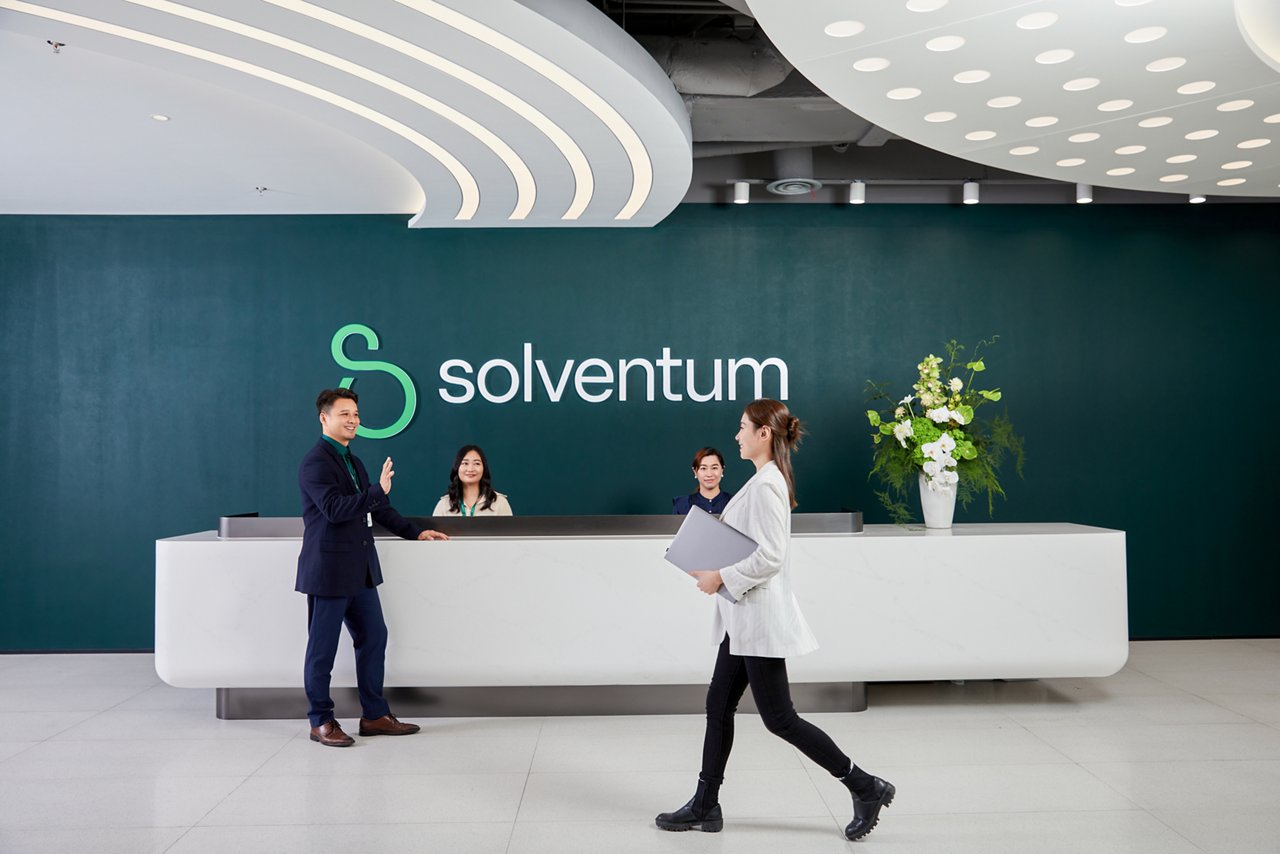 人們在明亮的 Solventum 辦公室大廳交流，其中有人走過接待櫃台。